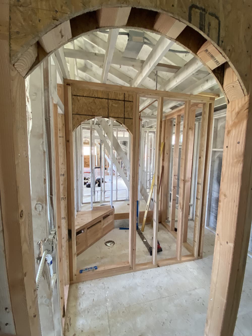 Interior framing seen through an arched opening, with a second arched opening beyond it, before any drywall.
